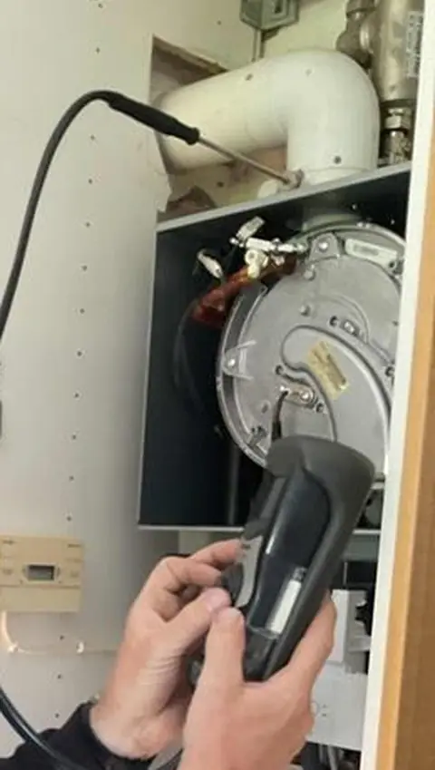 Engineer's hands holding a flue gas analyser at an open boiler
